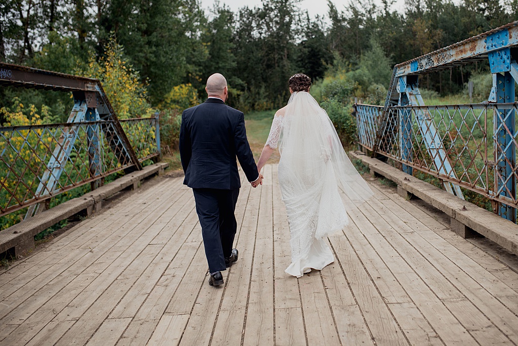 bride-groom-walking-away-on-bridge-holding-hands